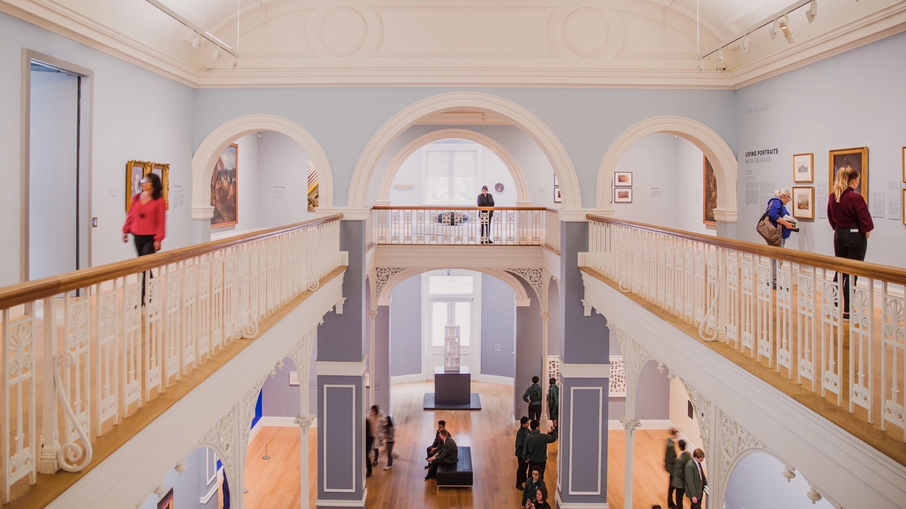 Interior view of people looking at art on two levels of Auckland Art Gallery Toi o Tāmaki. Image credit: Auckland Brand Library