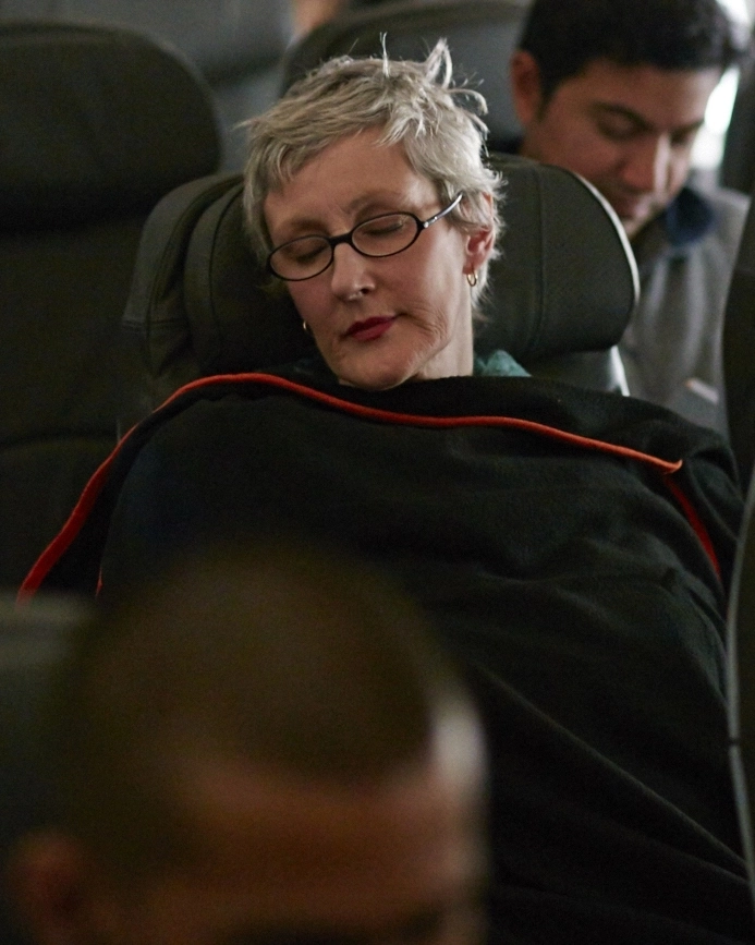 Woman asleep on a plane with a blanket over her
