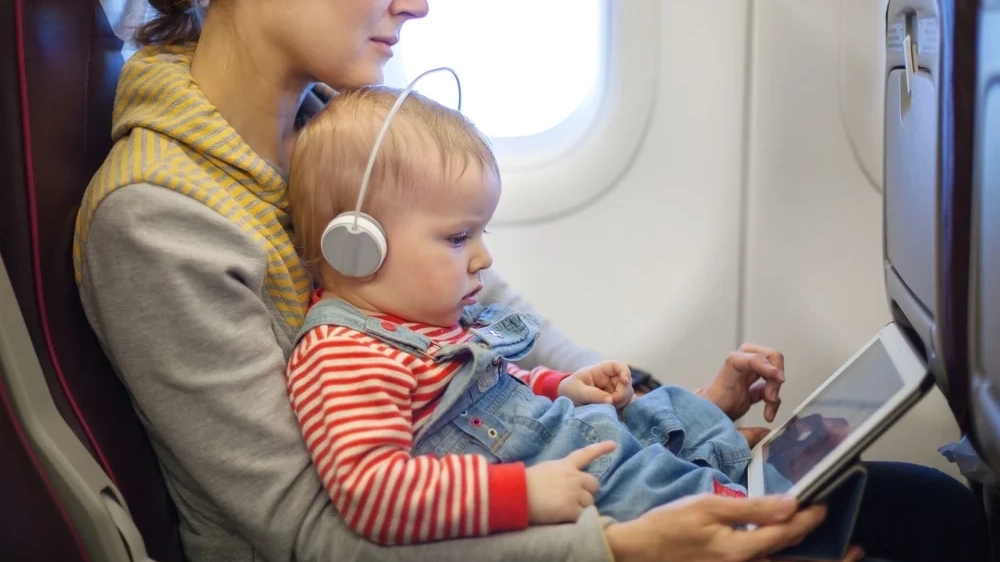 Baby on parent's lap wearing a wireless headphone while looking on a iPad.
