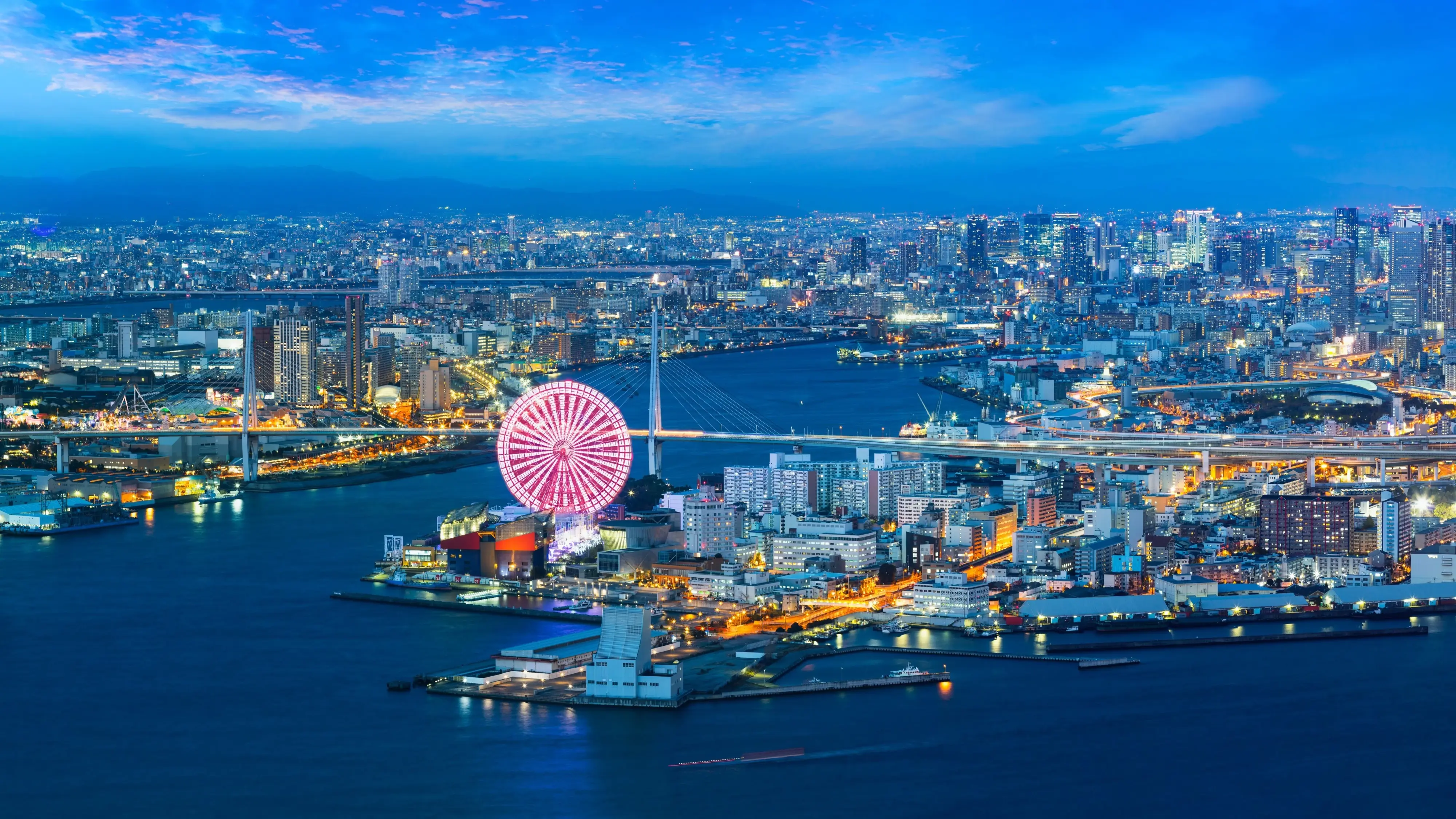 A panoramic nighttime view across Osaka Bay and city with lit up skyscrapers and Tempozan Giant Ferris Wheel. Image credit: stock.adobe.com