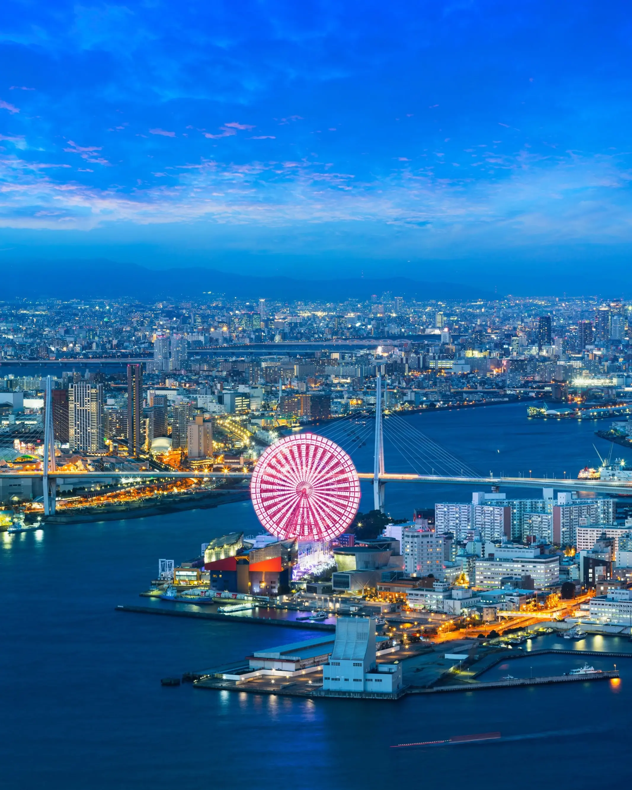 A panoramic nighttime view across Osaka Bay and city with lit up skyscrapers and Tempozan Giant Ferris Wheel. Image credit: stock.adobe.com