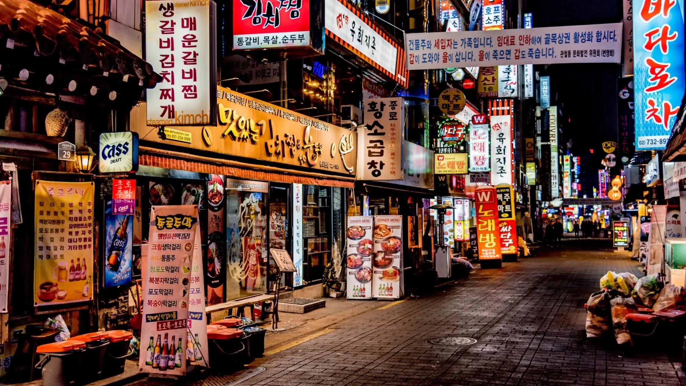 Lit up restaurant billboards with Korean writing at night in a laneway. Image credit: stock.adobe.com