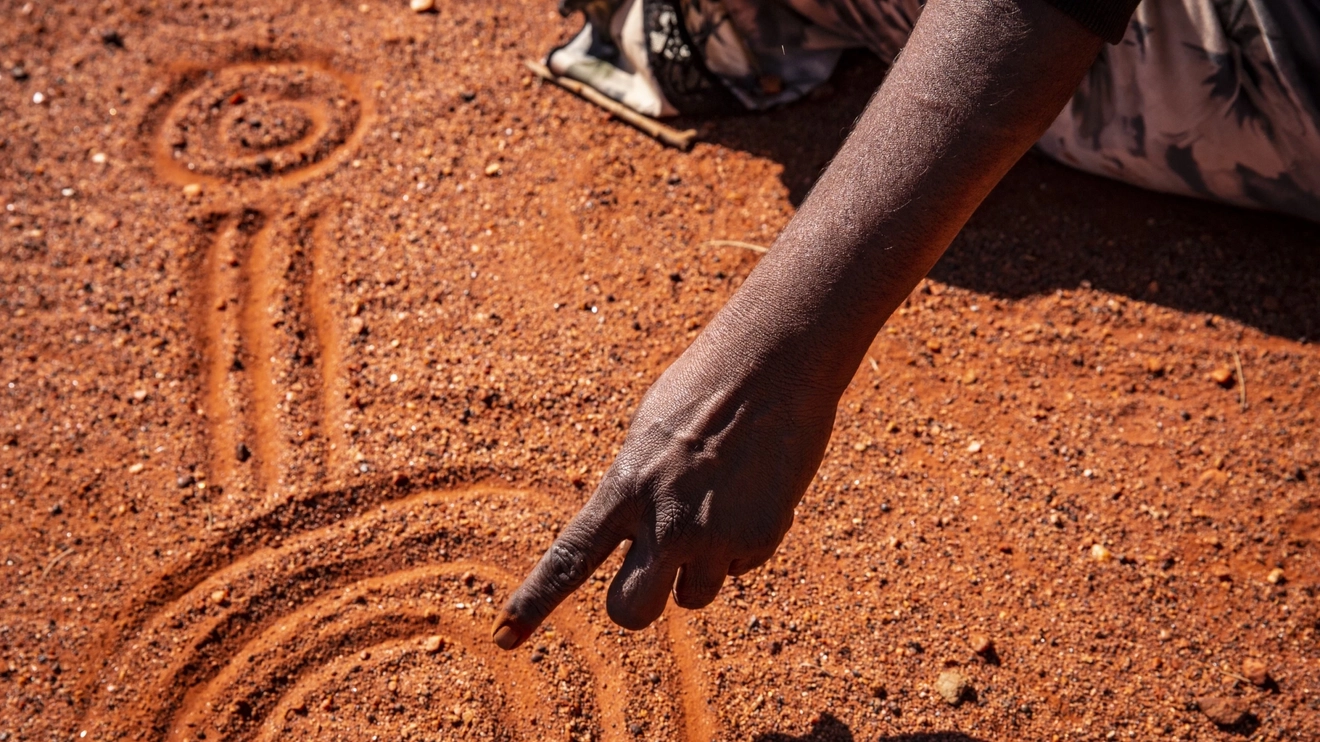 Artist pointing at sand drawing at Maruka Arts, Uluru. Image credit: Tourism NT/Archie Sartracom