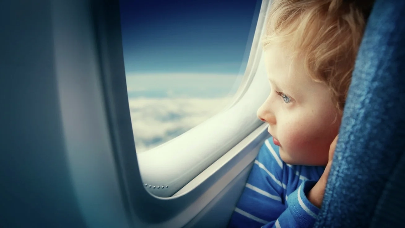 A kid looking outside at a window of an Airplane. Image credit: iStock