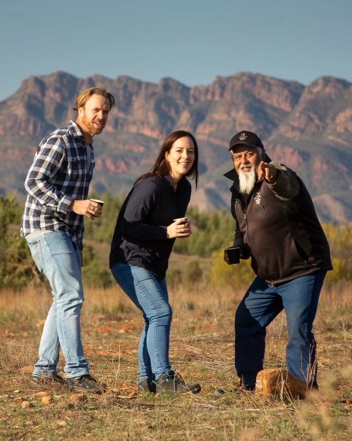 With Flinders Ranges in the background, First Nations guide points to something in the distance while two tourists look on. This is a wonderful area to experience Aboriginal Australia. Image credit: Tourism Australia.