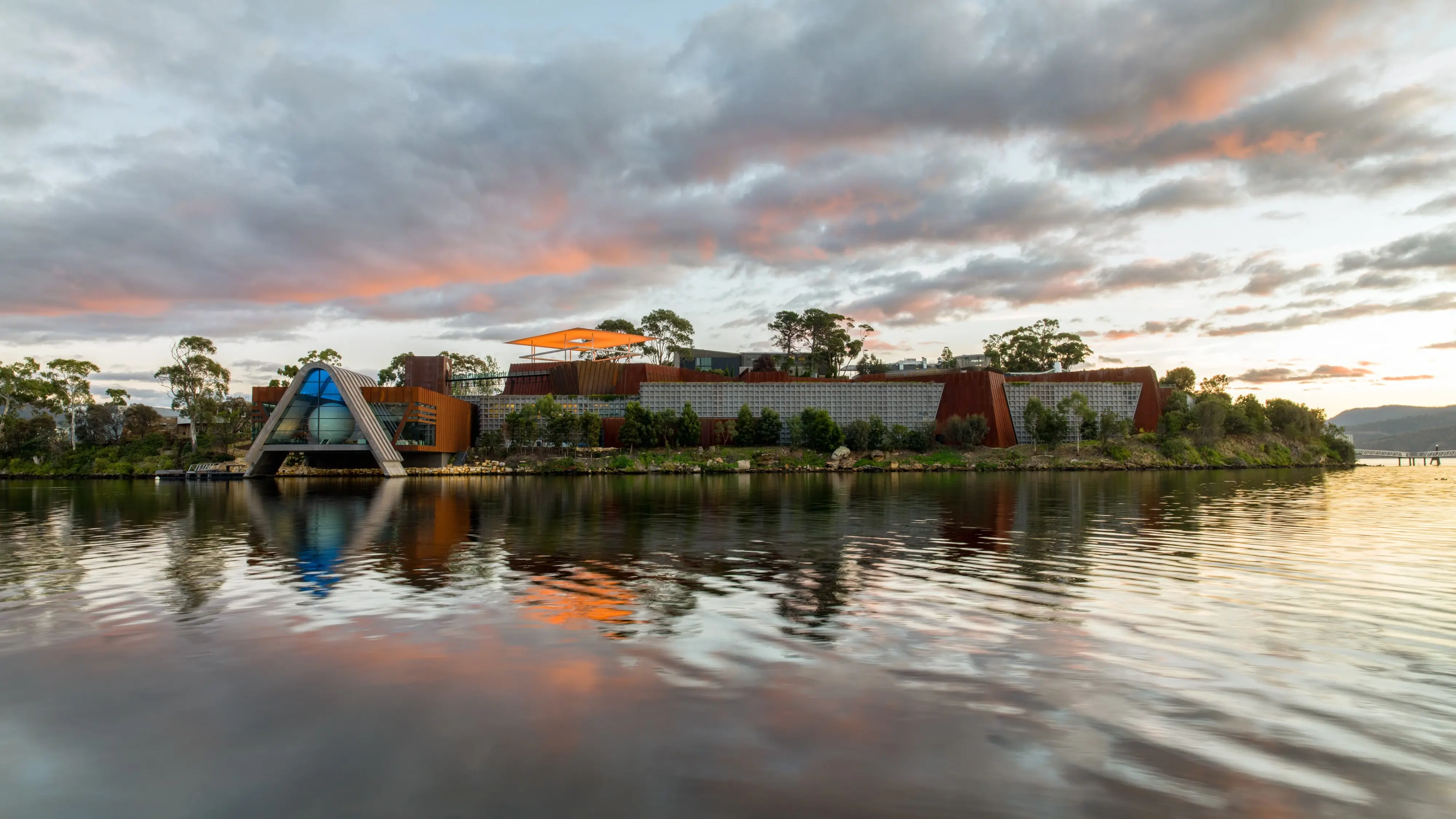 Geometric buildings of Mona with the Derwent River in the foreground and a sunset sky. Image credit: Mona/Jesse Hunniford