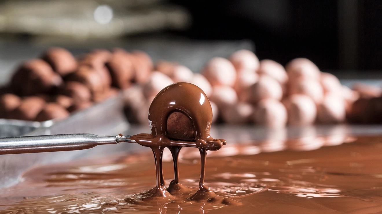 Close up of a chocolate ball being dipped in melted chocolate, chocolates in background, Haigh's, Adelaide. Image credit: South Australia Tourism Commission