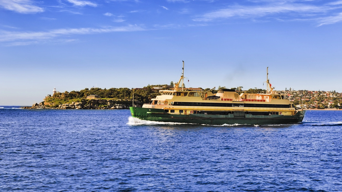 Passenger ferry travelling across Sydney Harbour with homes and a lighthouse in the distance. Image credit: taras vyshnya/shutterstock.com