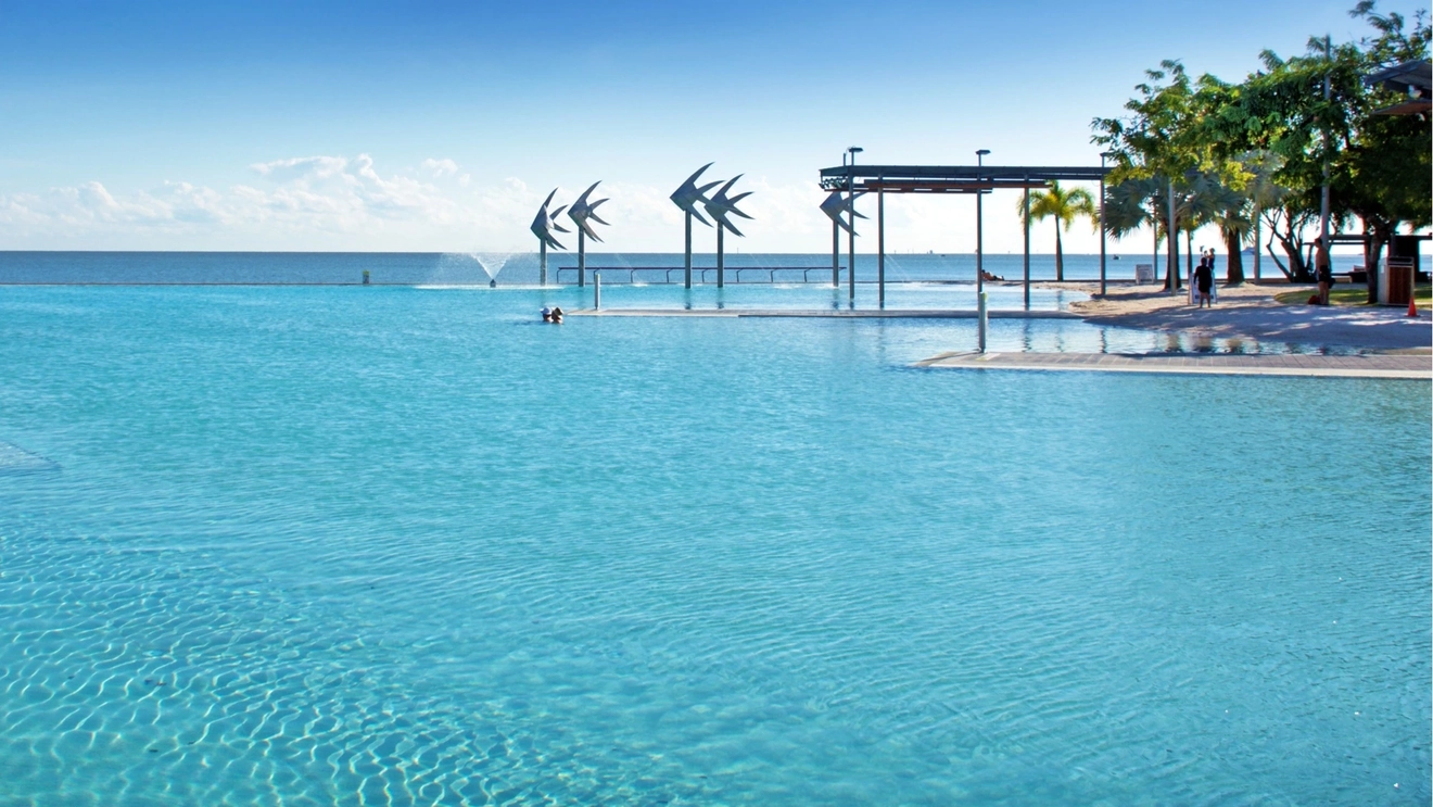 Saltwater Cairns Lagoon with swimmers, palm trees, sandy banks and ocean in background.