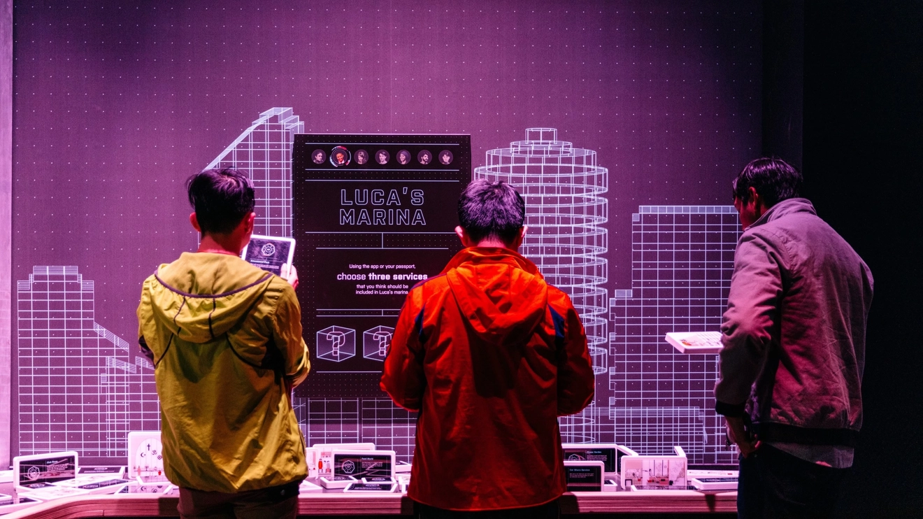 Back view of three people interacting with a display and screen that reads “Luca’s Marina” at MOD., University of South Australia, Adelaide. Image credit: South Australia Tourism Commission