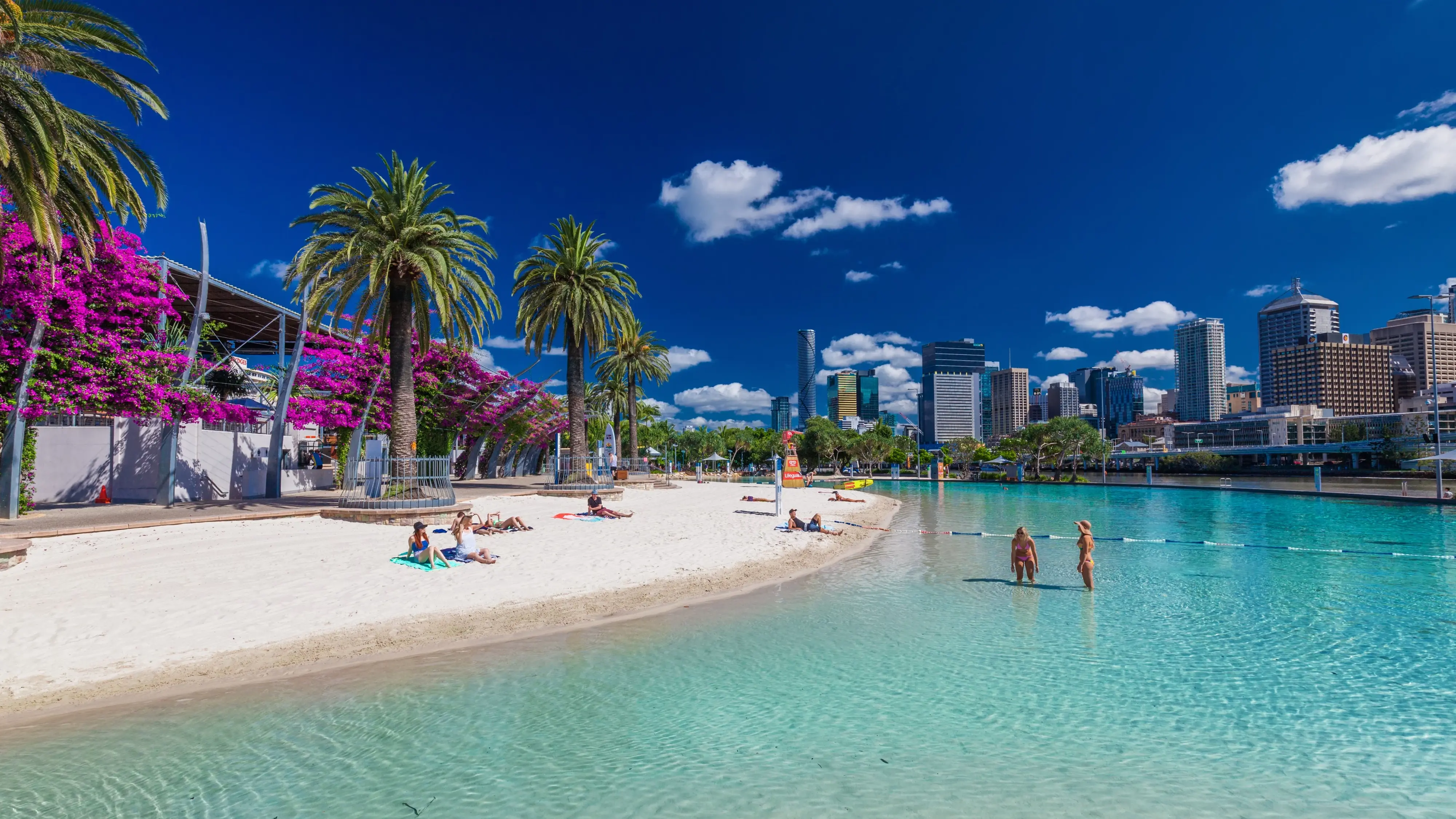 A man-made beach with sand and palm trees and the Brisbane CBD in the background. Image credit: Shutterstock