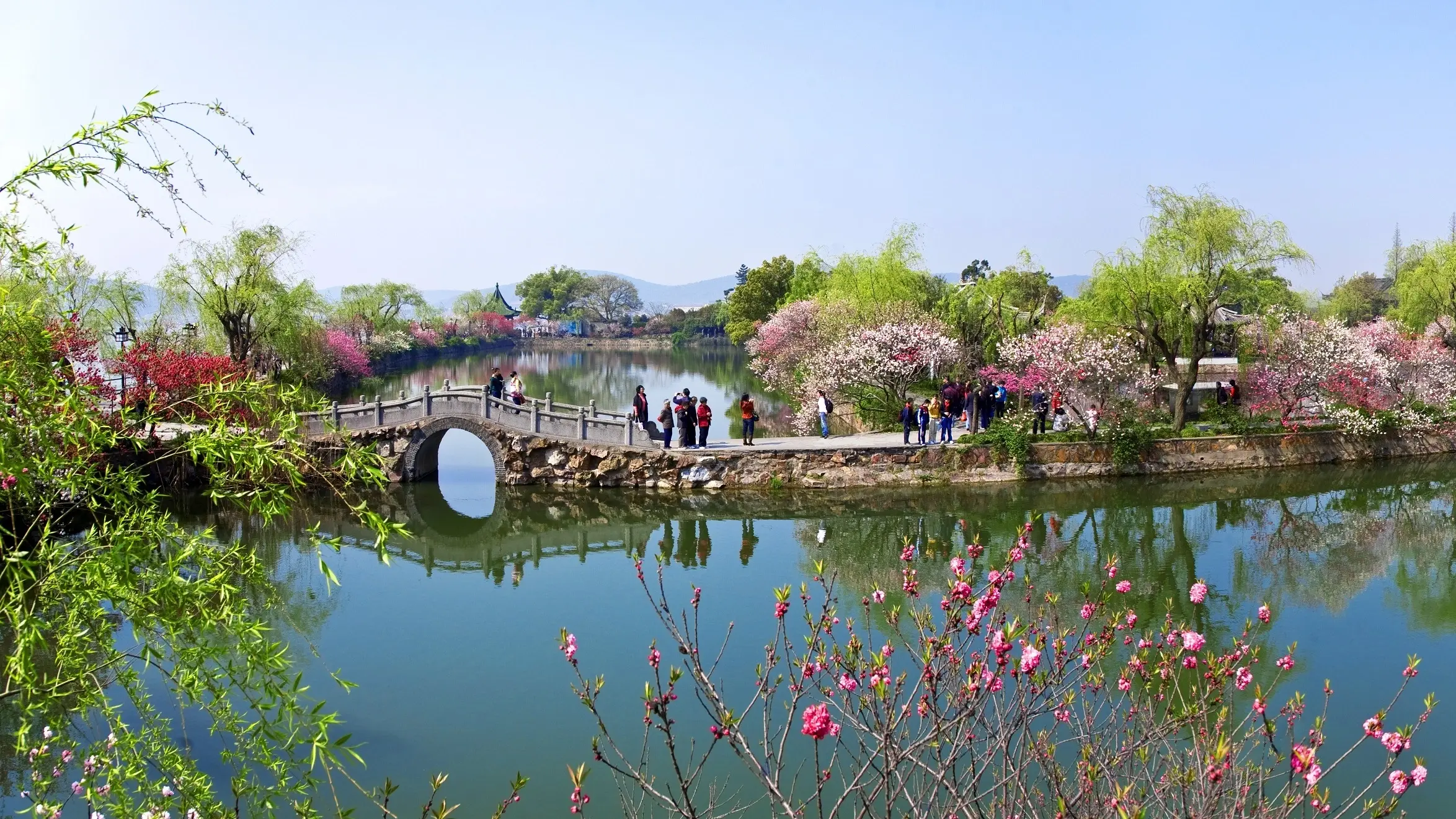 People on a footbridge and path flanked by Li Lake, with pagodas surrounded by blossoming trees, in Liyuan Gardens in spring, Wuxi, China. Image credit: Wuxi Tourism Board