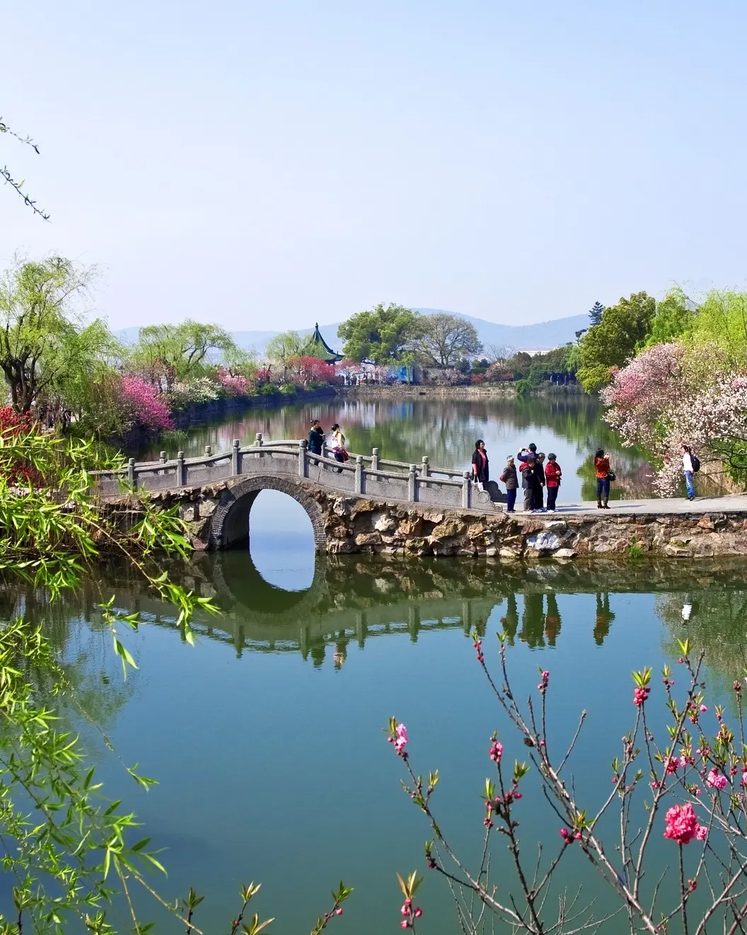 People on a footbridge and path flanked by Li Lake, with pagodas surrounded by blossoming trees, in Liyuan Gardens in spring, Wuxi, China. Image credit: Wuxi Tourism Board