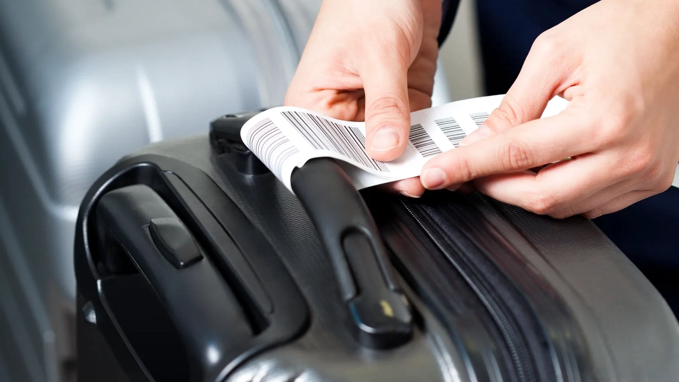 A man's hands attaching a bag tag to the handle of a black suitcase.