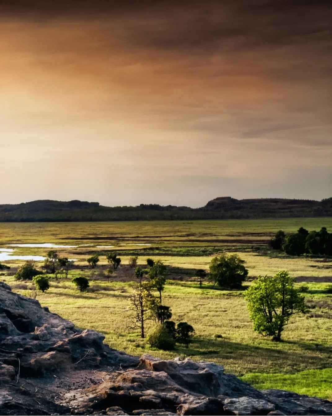 Solo traveller standing at Ubirr, Kakadu National Park, overlooking floodplains at sunset. 