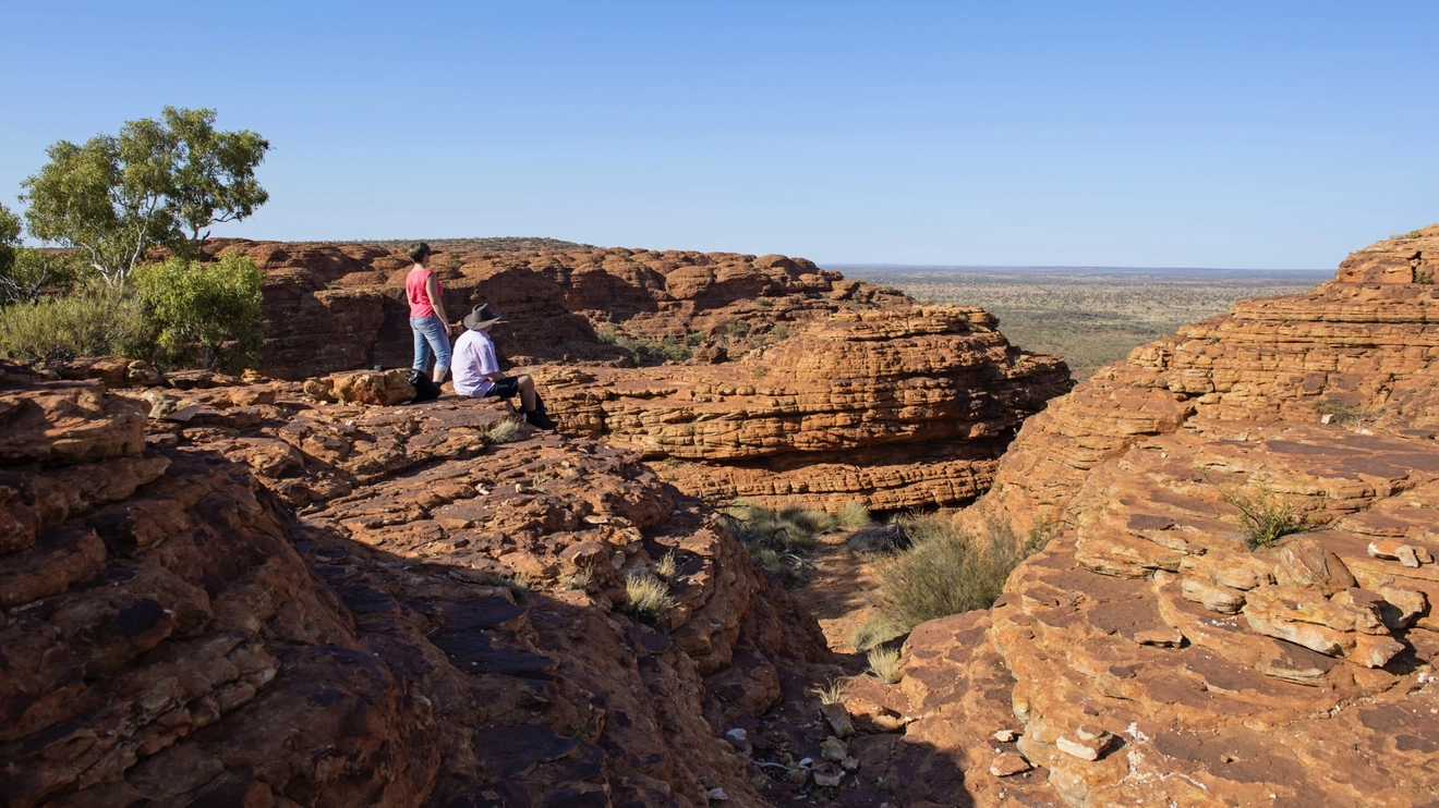 Two people looking into a valley from atop the rim at Kings Canyon, Watarrka National Park. Image credit: Tourism NT/Shaana McNaught