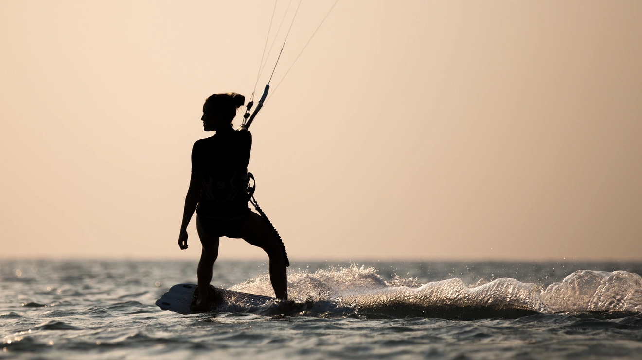 A silhouette of a person kiteboarding against a golden sunset sky. Image credit: Shutterstock
