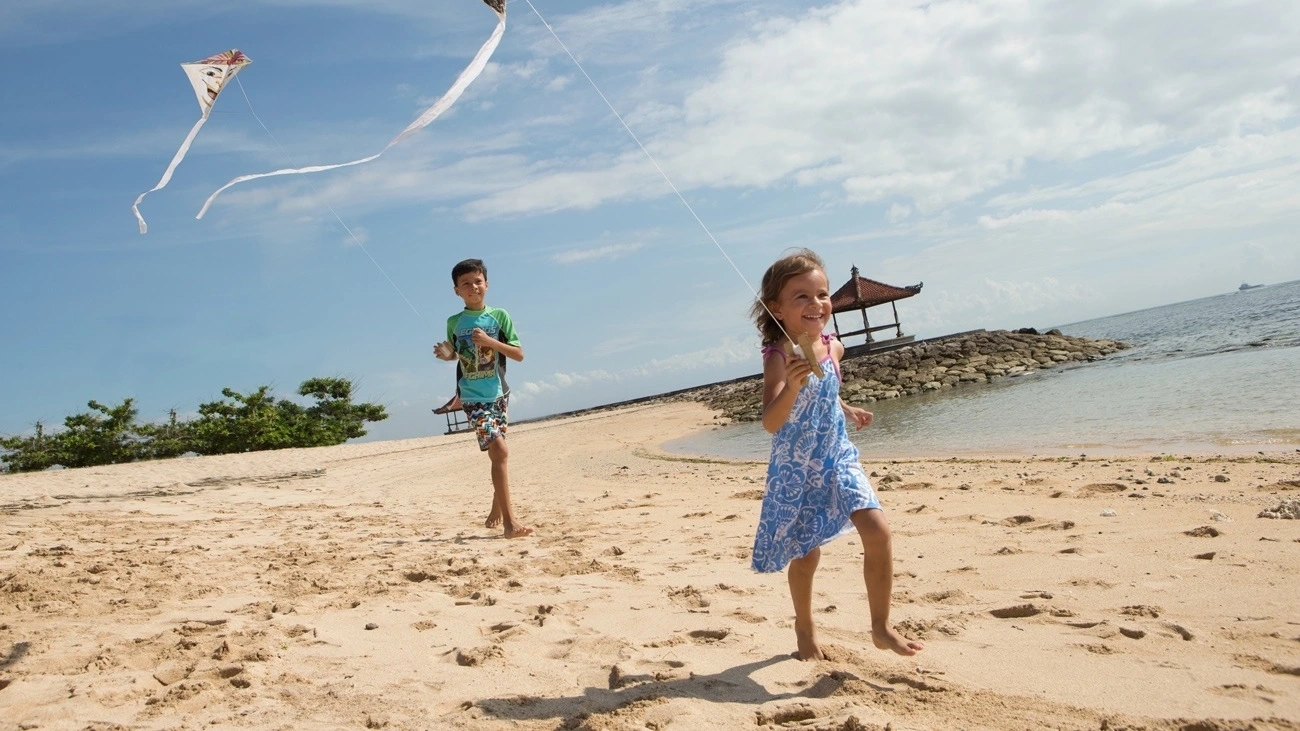 Two children run on the beach in Bali with kites