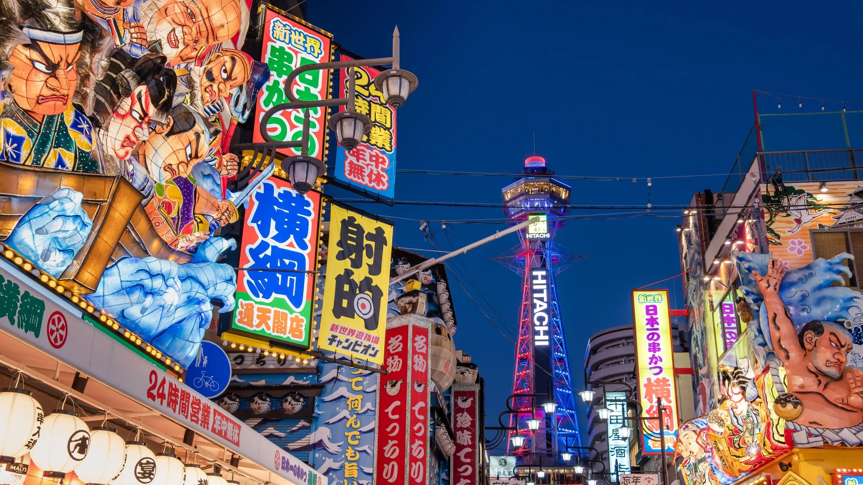 Illuminated neon signs and Tsutenkaku Tower in Shinsekai, Osaka, at night. Image credit: pinglabel – stock.adobe.com