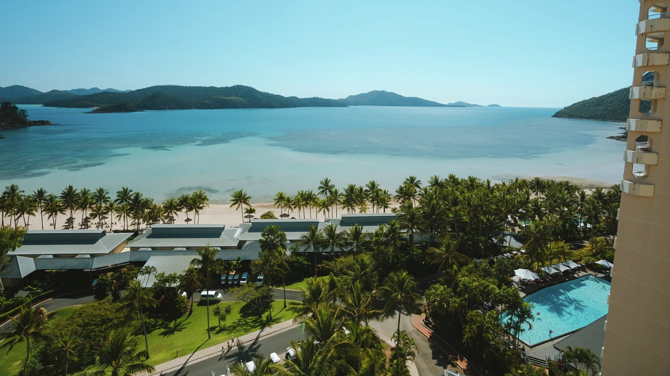 View from Reef View Hotel looking out over swimming pool, buildings, palm trees, beach, water and islands. Image credit: Tourism and Events Queensland