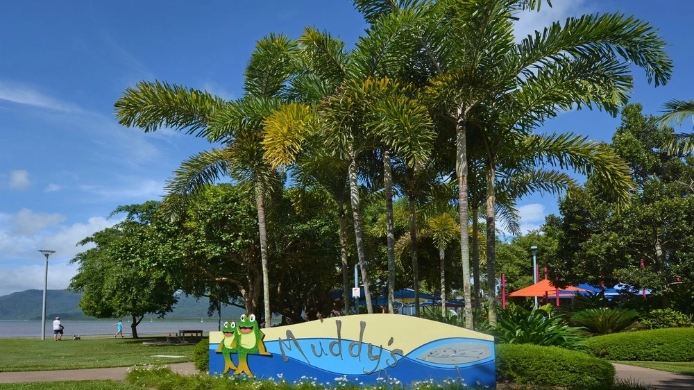 Sign at the entrance to Muddy's Playground, Cairns, backed by large palm trees.