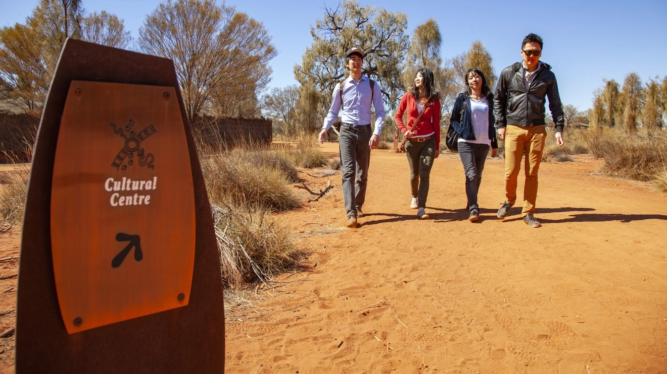 Four people walking on a track with Uluru Cultural Centre sign in foreground. Image credit: Tourism NT