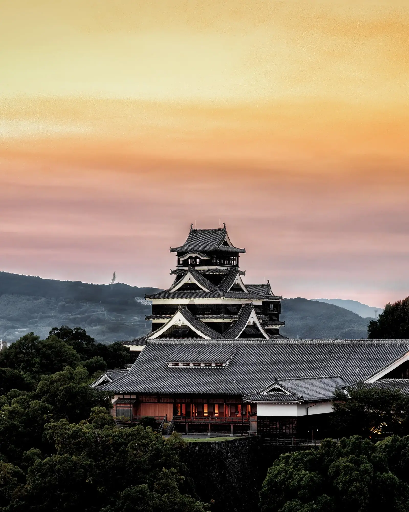 Kumamoto Castle, surrounded by trees, with Kumamoto city skyline and mountains in backround, at sunset. Kumamoto, Kyushu, Japan. Image credit: stock.adobe.com