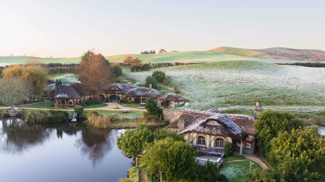 Aerial view of Hobbiton movie set surrounded by green fields lightly covered in snow.
