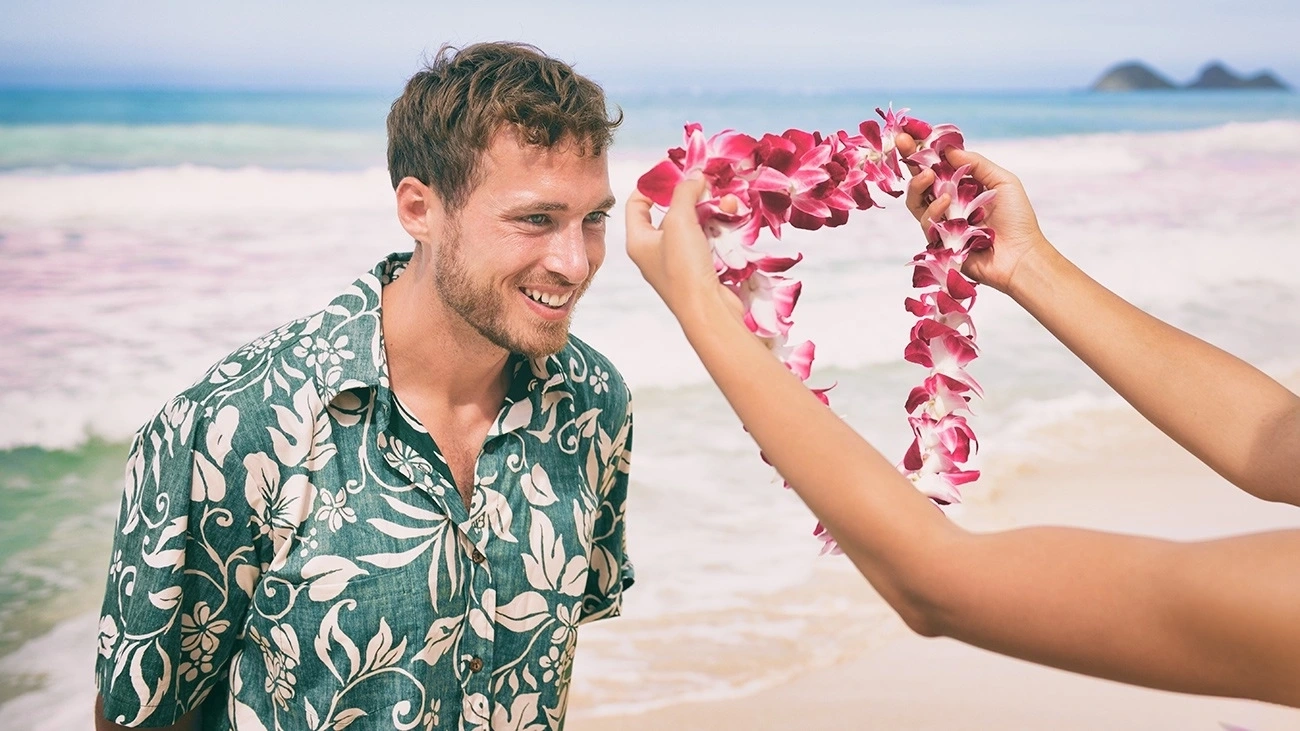 A woman puts a lei on a man wearing a Hawaiian shirt.