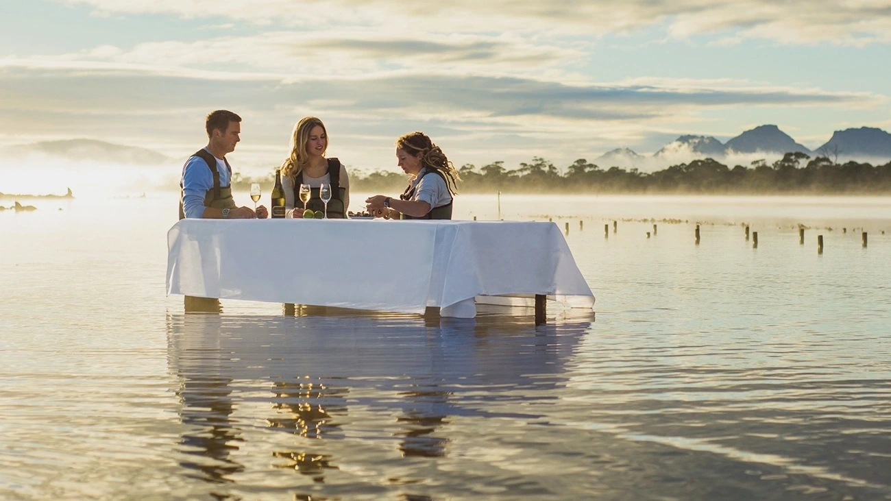 People tasting seafood at a table in the water at Freycinet Marine Farm.