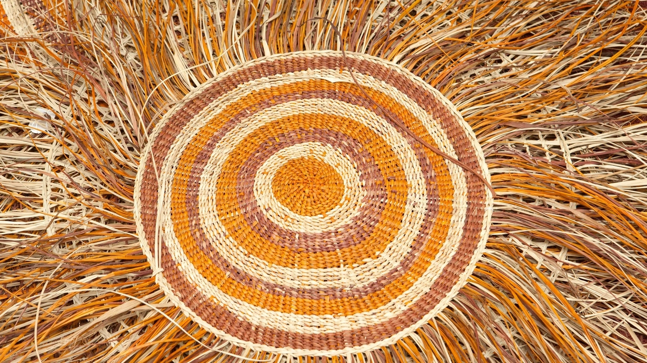 A close up of a spiral weaving in yellow, orange and brown. Image credit: Tourism NT/Mason Art Gallery