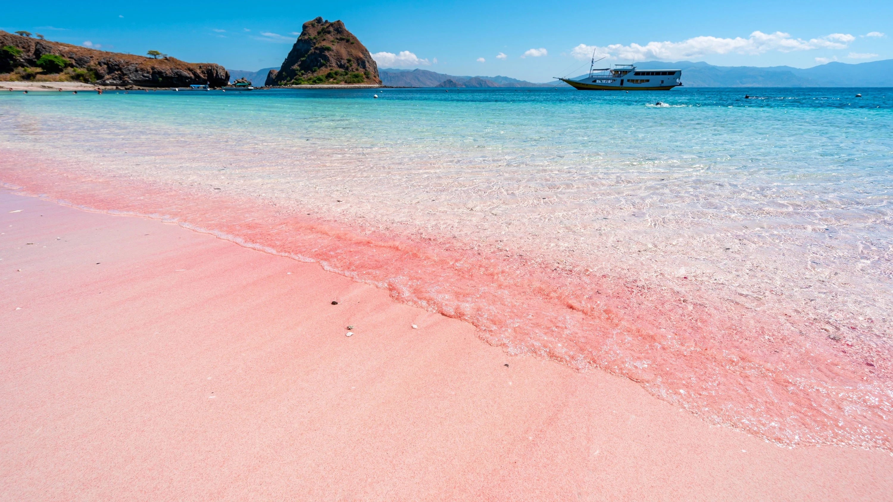 Pristine pink sand beach in Komodo National Park, Labuan Bajo. A phinisi boat floats on the aquamarine water. Image credit: stock.adobe.com