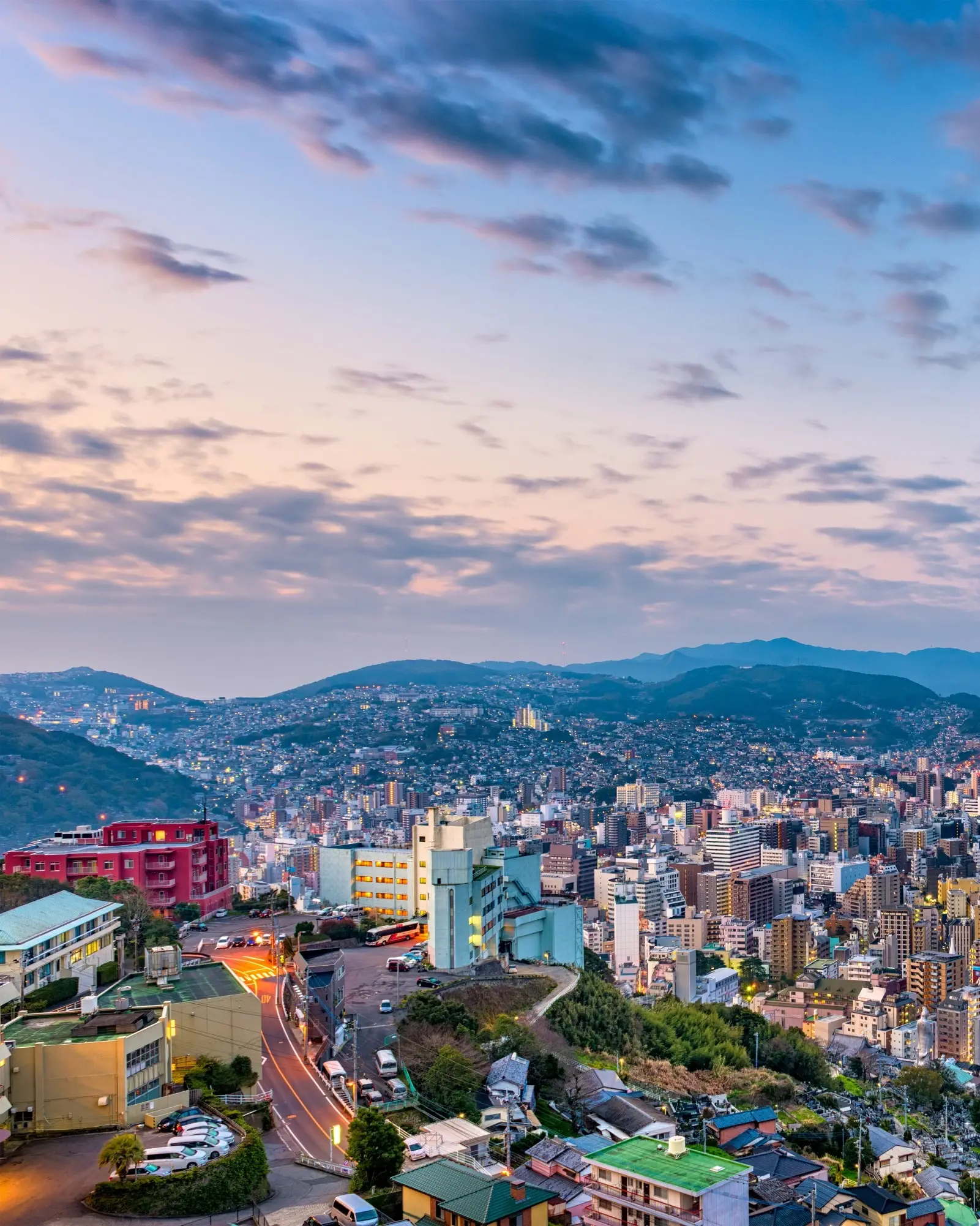 Aerial view of Nagasaki's skyline at dusk, with tall buildings in the foreground, a river and mountains in the background. Image credit: stock.adobe.com