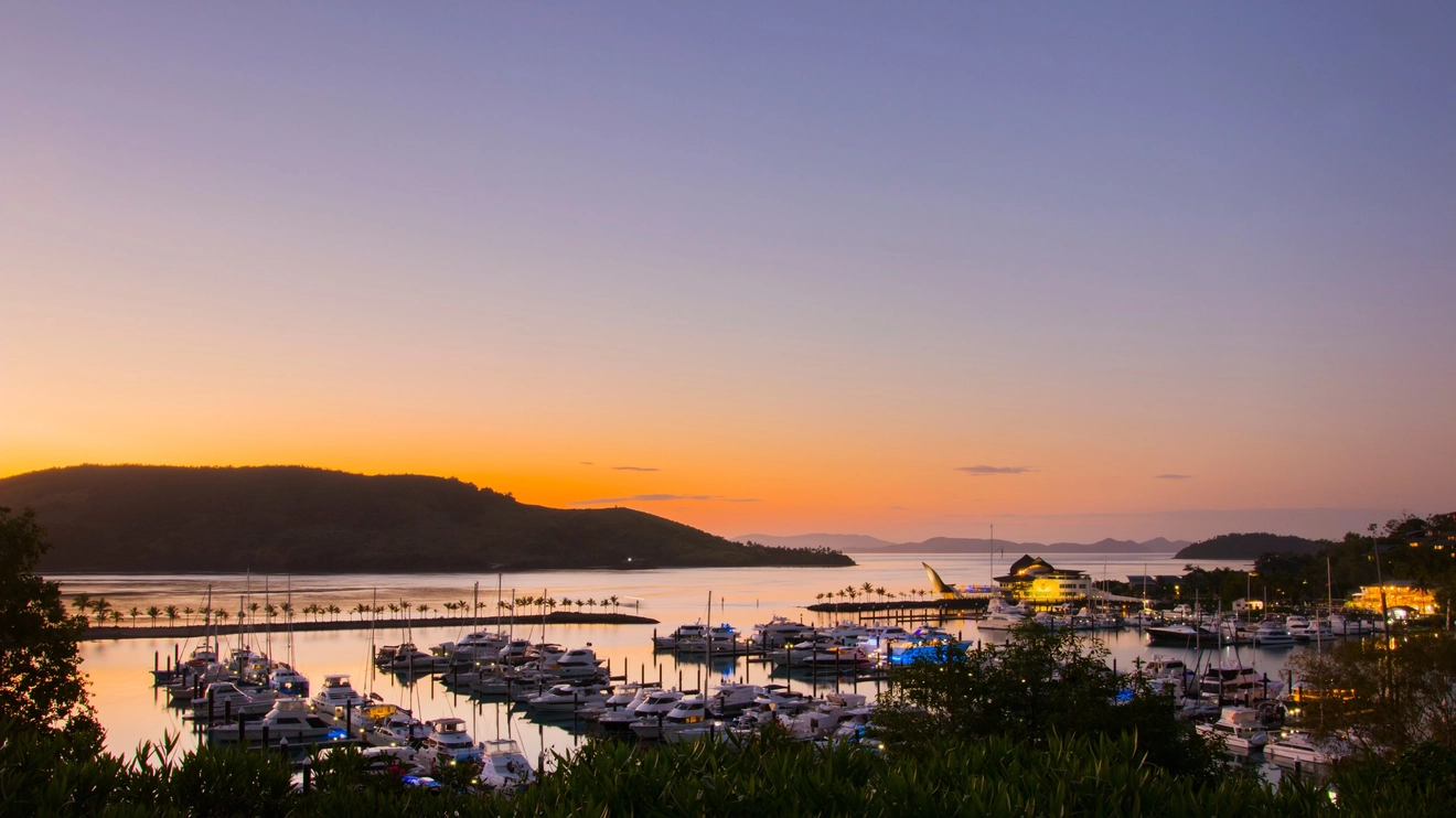 The lights of the Hamilton Island Marina at sunset with a hill in the background. Image credit: Shutterstock