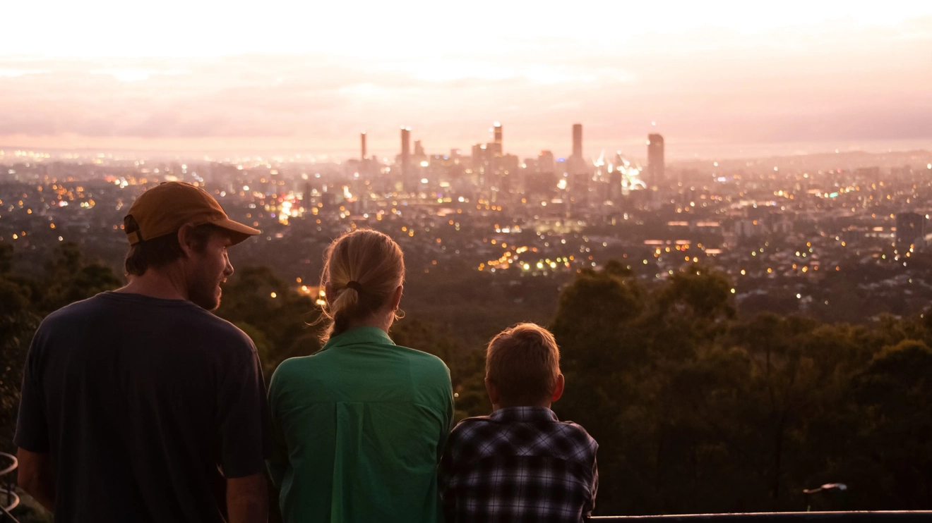 Back view of three people at the Mt Coot-tha Lookout, with the Brisbane skyline in the distance. Image credit: Tourism and Events Queensland