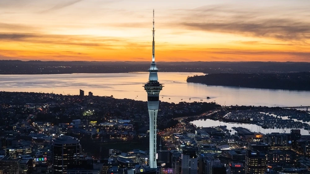 Aerial view of Auckland city skyline at night with SkyCity tower in foreground and harbour in background.