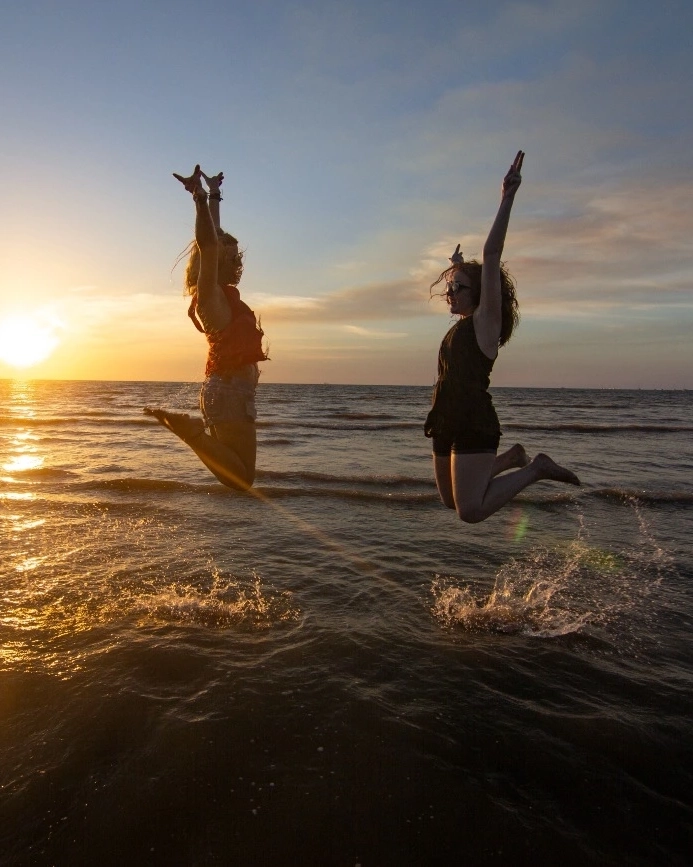 Two women jumping out of the water on the beach at Casuarina at sunset, Darwin, Northern Territory. Image credit: Tourism Australia/Allan Dixon