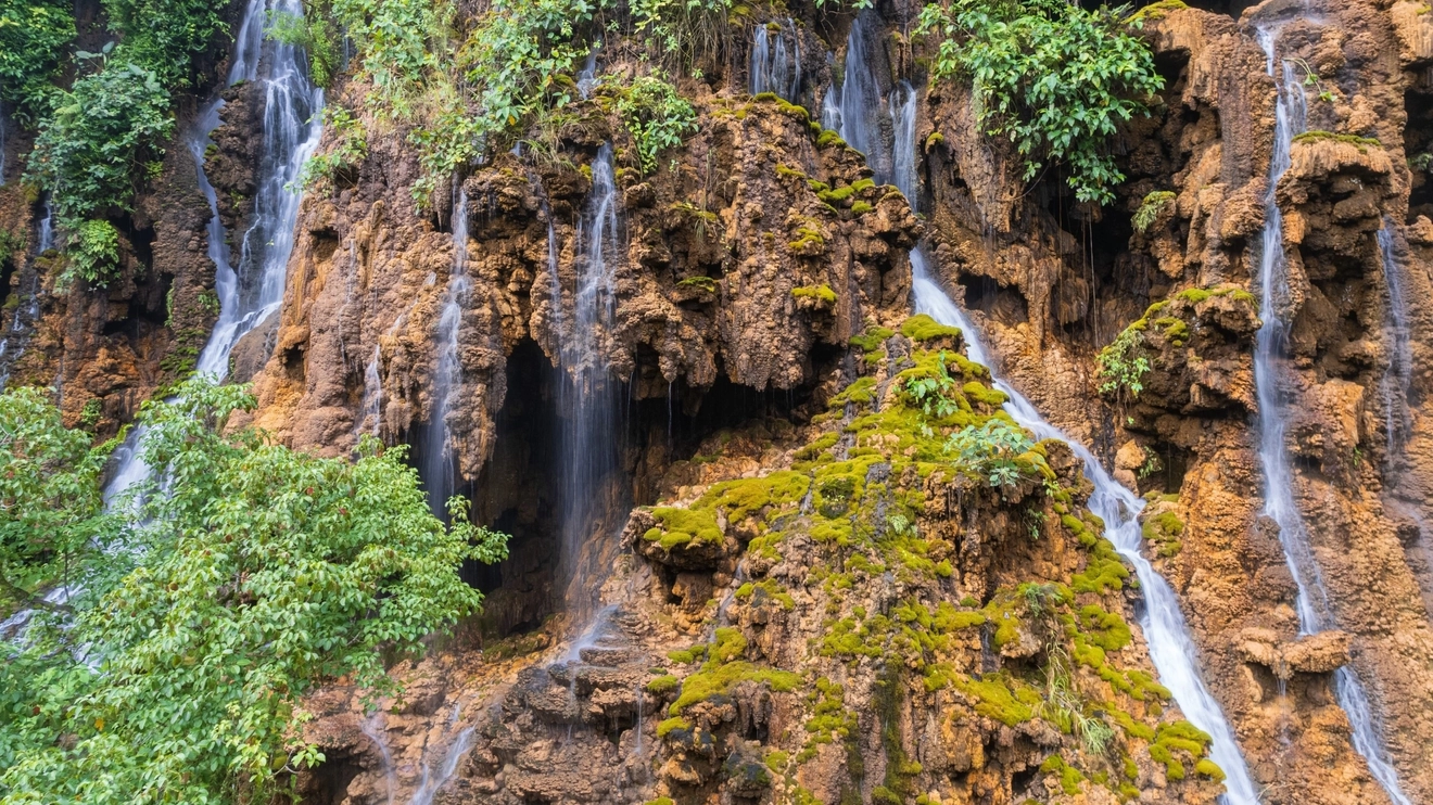 Small waterfalls cascade over cave openings, rocks and greenery at Goa Tetes, East Java. Image credit: stock.adobe.com