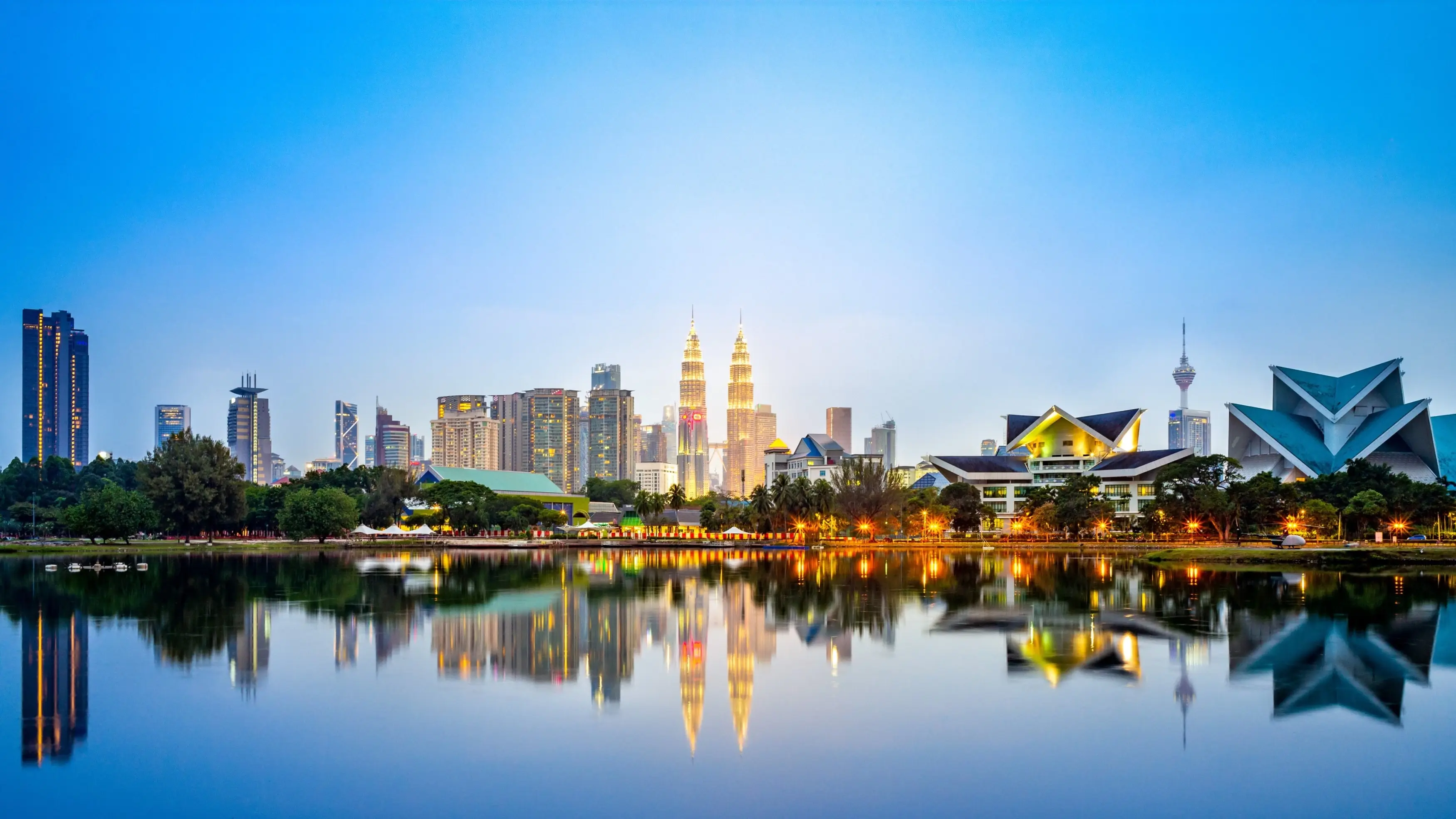 Kuala Lumpur's city skyline at night, with lights reflecting on the lake in the foreground. Image credit: stock.adobe.com