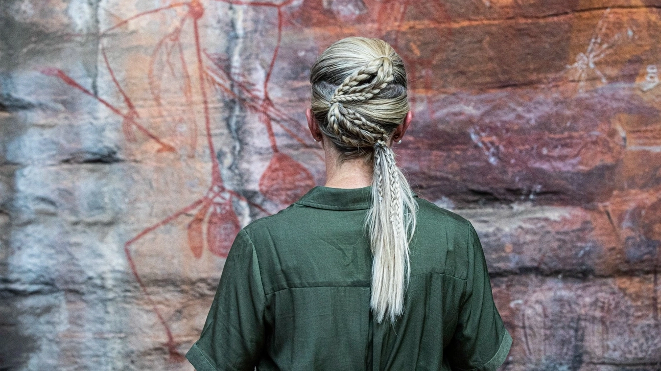 Young blonde woman looks at ancient Aboriginal rock art, Ubirr (Kakadu National Park). Image credit: Tourism NT/Helen Orr